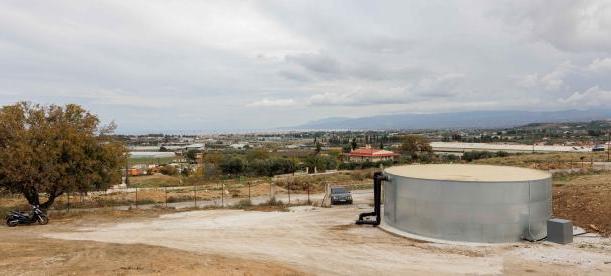 Wide view of a rural landscape with a circular water tank in the foreground, surrounded by dirt paths and sparse vegetation.